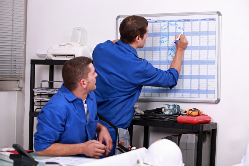 Zwei Handwerker tragen Termine in eine Plantafel ein